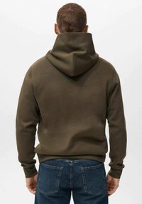 Olijfgroene hoodie met een trekkoordcapuchon en een gladde, zachte textuur. Heeft een relaxte pasvorm en geribbelde manchetten, gecombineerd met blauwe spijkerbroek.