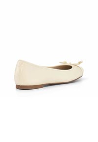 Danseuse en cuir crème, avec un bout rond, un petit nœud en accent et une finition lisse. Dispose d'une semelle plate brun clair.