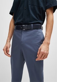 Chemise bleu marine à manches courtes associée à un pantalon bleu clair. Une ceinture noire avec une boucle argentée complète l'ensemble. Texture de tissu lisse.