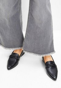 Ballerine in pelle nera a punta con una cintura decorativa sulla parte superiore. Indossate con pantaloni in denim grigio larghi con orli sfilacciati.