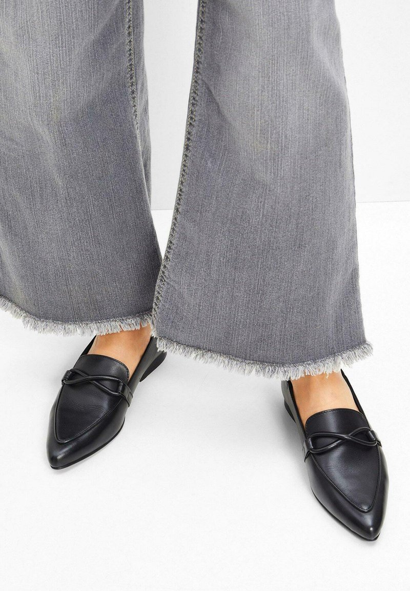 Ballerine in pelle nera a punta con una cintura decorativa sulla parte superiore. Indossate con pantaloni in denim grigio larghi con orli sfilacciati.