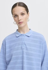 Polo shirt azzurro chiaro con un design testurizzato a righe orizzontali, colletto e pattina con bottoni. Tessuto morbido a maglia.