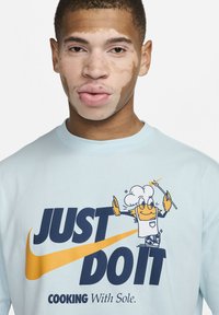 Un t-shirt à manches longues bleu clair avec un grand texte "JUST DO IT" en marine, accompagné d'un graphique de chef de dessin animé et de "COOKING With Sole."