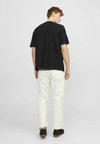 Tricou negru cu mâneci scurte, asortat cu pantaloni cargo de culoare crem, având o croială lejeră, manșete răsucite și detalii discrete ale buzunarelor.