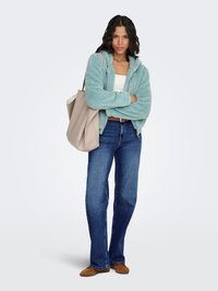Light blue, fuzzy hooded jacket over a white top, paired with dark blue jeans and brown shoes. A large beige tote bag is slung over one shoulder.