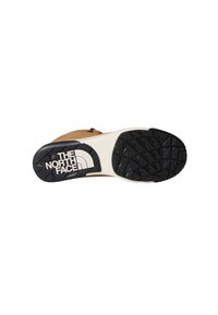 Chaussure marron avec une semelle en caoutchouc noire texturée. La semelle présente un motif triangulaire et affiche bien en évidence la marque "THE NORTH FACE".