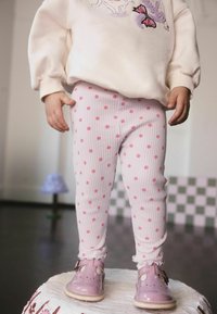 Felpa bianca con un'illustrazione, leggings rosa a costine con pois rosa e scarpe rosa chiaro con cinturino e dettagli traforati.