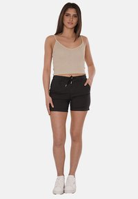 Pantaloni sportivi neri con vita regolabile e due tasche frontali, abbinati a un crop top beige a coste. Il modello assume una posa neutra indossando scarpe da ginnastica bianche.