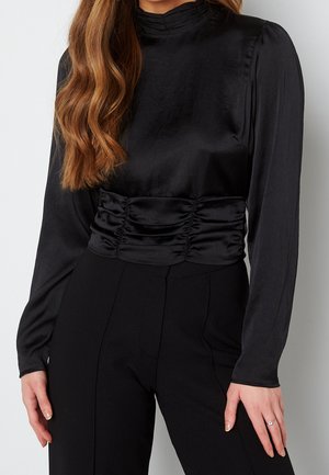 Top lungo a maniche corte in satin nero con collo alto e dettagli arricciati in vita, caratterizzato da una texture liscia e un design aderente.