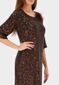 Brązowa sukienka cekinowa z krótkimi rękawami, o strukturalnej fakturze i z piórowym akcentem przy dekolcie. Elegancki i dopasowany fason.