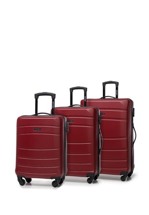 Trois valises rigides rouges de tailles variées, avec une finition texturée, des poignées noires et des roues lisses.