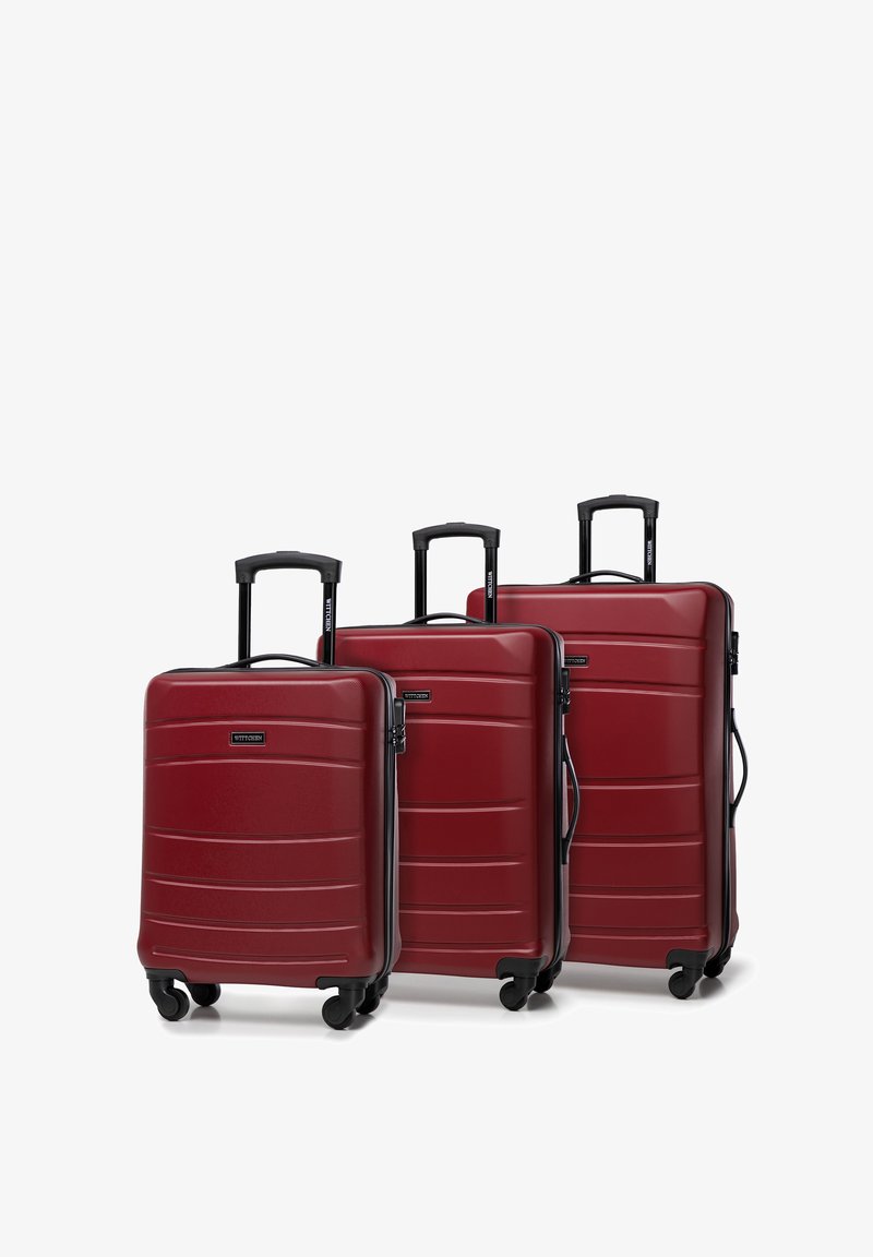 Tre valigie rigide rosse di diverse dimensioni, con una finitura texture, maniglie nere e ruote che scorrono senza sforzo.