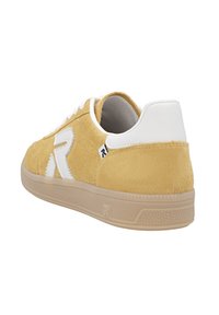 Baskets en daim jaune avec des accents blancs et des lacets blancs, présentant un bout arrondi et une semelle en caoutchouc texturée. Détail du logo sur le côté.