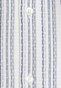 Gestreept shirt met een wit en blauw patroon. Het heeft een textuurstof en witte knopen met vier gaten. Verticale strepen zijn gelijkmatig verdeeld.