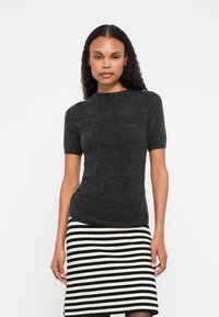 Μαύρη πλεκτή μπλούζα με κοντό μανίκι και εφαρμοστή γραμμή, με στρογγυλή λαιμόκοψη και λεία υφή, συνδυασμένη με μια φούστα με λευκές και μαύρες ρίγες.