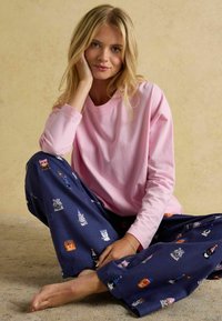 Světle růžová košile s dlouhým rukávem spárovaná s námořnickými vzorovanými pyžamovými kalhotami s barevnými potisky zvířat v party kloboucích. Měkká tkanina, volný střih.