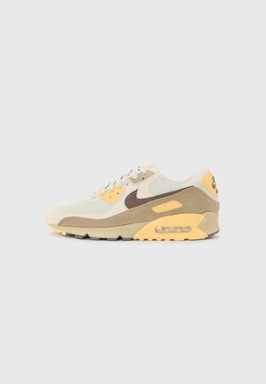 Tenisky Nike Air Max 90 s béžovým zvrškom, hnedými akcentmi, žltými detailmi a viditeľnou vzduchovou jednotkou v päte. Gumová podrážka dotvára dizajn.