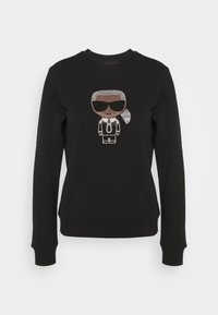 Svart sweatshirt med en glittrande rhinestonesgrafik av en person med solglasögon, designad med rund halsringning och ribbad mudd.