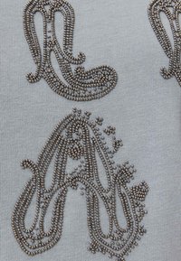 Perlage métallique complexe formant des motifs cachemire décoratifs sur un tissu tricoté gris clair.
