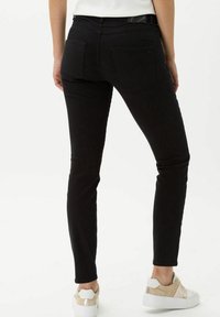 Jeans negros de corte slim con bolsillos traseros, cintura a media altura y una textura suave. Llevados con zapatillas blancas y beige.