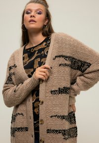 Strickjacke in Beige mit schwarzen Tiermusterakzenten, die einen lockeren Schnitt, Knopfverschluss und gerippte Bündchen aufweist. Texturierter Stoff.