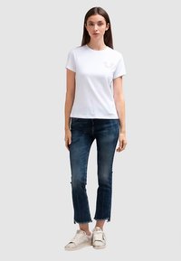 Biały bawełniany t-shirt z krótkimi rękawami, z małym różowym logo na piersi; w zestawie z niebieskimi krótkimi jeansami i białymi tenisówkami.