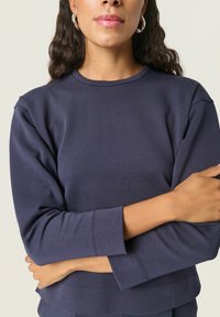 Sudadera azul marino con escote redondo, mangas largas y puños acanalados. Textura suave y detalles de costura mínimos.