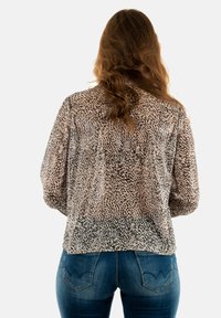 Blusa trasparente con un motivo leopardato in tonalità beige e marrone, abbinata a jeans blu con un design curvo della tasca posteriore.