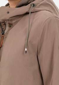 Chaqueta marrón con capucha, cremallera, cordón ajustable y tejido texturizado. Incluye un acento de cuero cerca del cierre y botones a presión.
