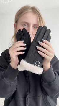 Fekete kesztyű puha fehér szőrme béléssel a mandzsettán, csattal díszítve. A kesztyűk sima textúrával és strukturált dizájnnal rendelkeznek.