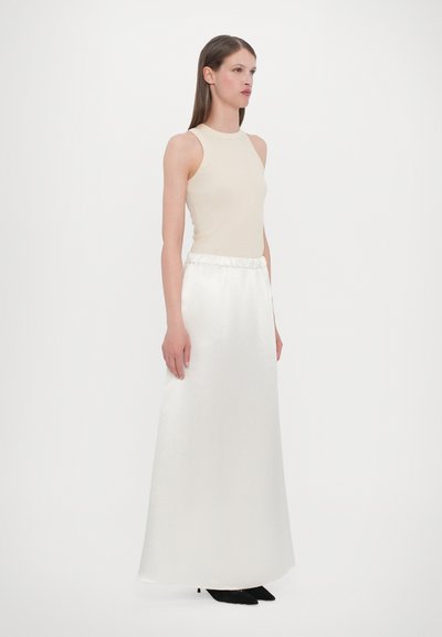 Utenermet beige topp kombinert med langt hvitt satin skjørt med elastisk midje. Svart hælhæl kompletterer antrekket.
