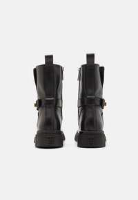Bottines en cuir noir avec une texture lisse, détail de fermeture éclair, accents de boucles et talons carrés arborant un logo en relief sur la semelle.