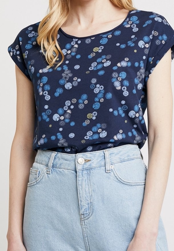 Femme portant un haut à manches courtes bleu marine avec un motif de formes circulaires bleues et claires, associée à un jean taille haute bleu clair.