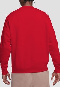 Sweat-shirt rouge avec un col rond, des manches longues, et des poignets et ourlets côtelés. La texture du tissu semble douce et lisse.