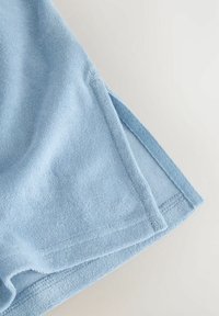 Lyseblåt håndklæde med blød tekstur, der har en pæn kant og diskrete sømdetaljer. Stofoverfladen er fyldig og absorberende.