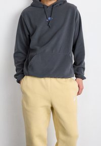 Grå fleecehuva med en känguruficka och justerbar snörning på huvan, kombinerad med gula svettbyxor med en liten logotyp.