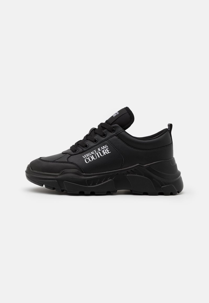 Baskets épaisses noires avec semelle épaisse et lacets, avec le logo blanc "Versace Jeans Couture" sur le côté.