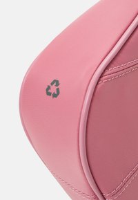 Różowa torba ekologiczna o gładkiej fakturze, z wyściełanymi brzegami i szarym symbolem recyklingu. Posiada delikatne szycie wzdłuż szwów.