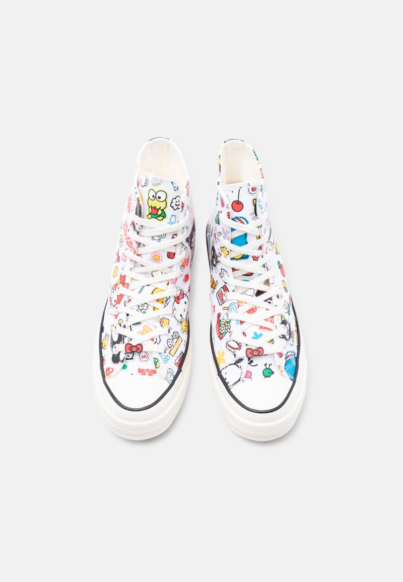 Zapatillas blancas de caña alta con patrones coloridos de personajes de dibujos animados y cordones blancos, vistas desde arriba sobre un fondo liso.