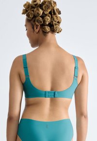Turkis bh med justerbare stropper, en glat tekstur og en hægte-og-øje lukning. Designet har en lav ryg og en minimalistisk stil.