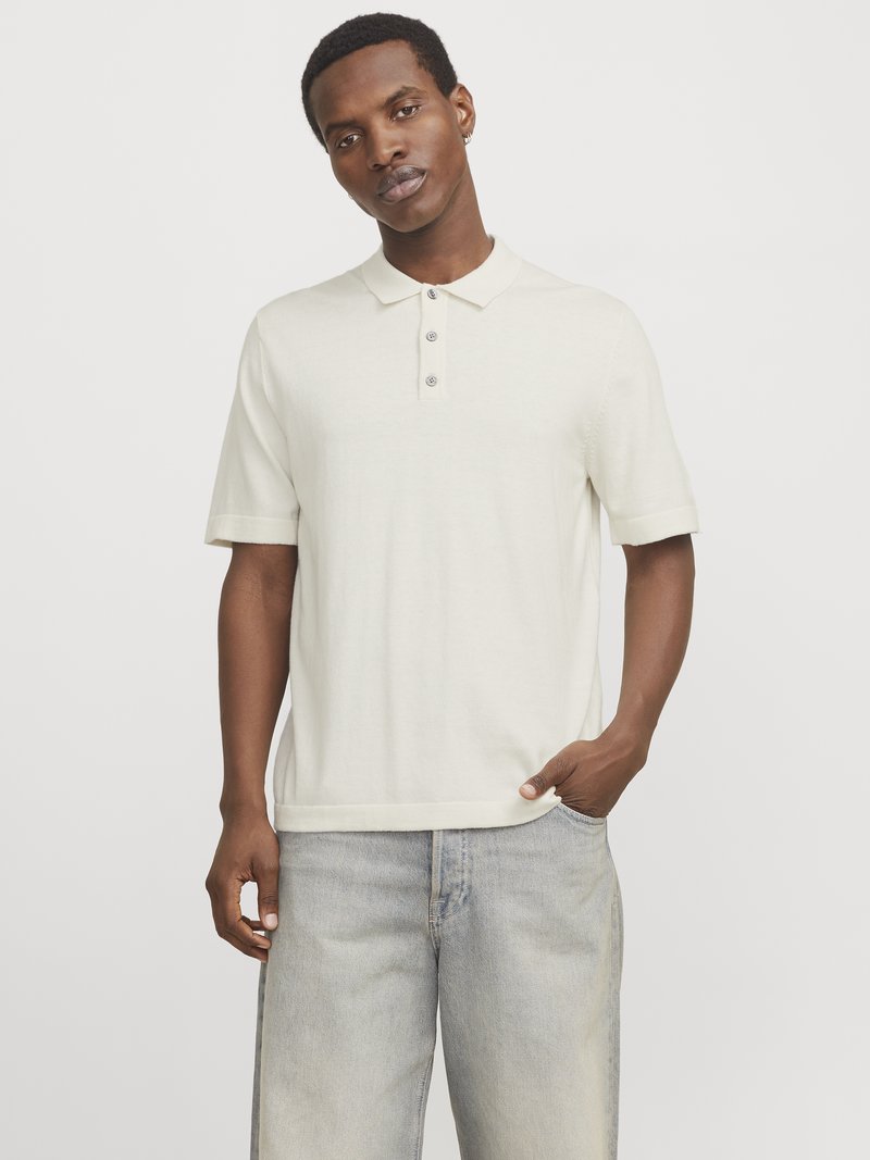 Polo crème à manches courtes avec un col et trois boutons, associé à un jean bleu clair à coupe décontractée. Texture lisse.