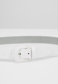 Hvid læderbælte med en glat finish og en sølvmetal spænde, der har justeringshuller og en let tekstureret grå underside.