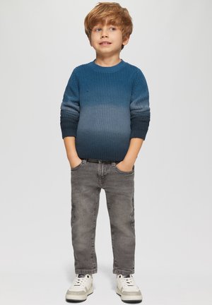 Sweter w kolorze gradientowego niebieskiego, wykonany z dzianiny, o prążkowanej fakturze i okrągłym dekolcie. Połączony z szarymi dżinsami i białymi trampkami.