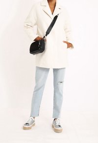 Weißer Fleece-Mantel mit Kragen, hellblaue ausgewaschene Jeans und silberne Plateausneaker. Schwarze Umhängetasche mit strukturierten Akzenten.