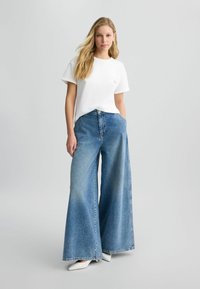 T-shirt en coton blanc à manches courtes et col arrondi, associé à un jean en denim bleu clair, à jambes larges, maintenu à la taille par un bouton.