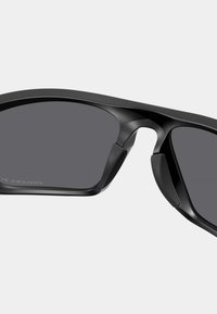 Lunettes de sport noires au design élégant et anguleux, avec des verres foncés et des accents en caoutchouc texturé sur les branches pour une meilleure prise en main et un confort optimal.