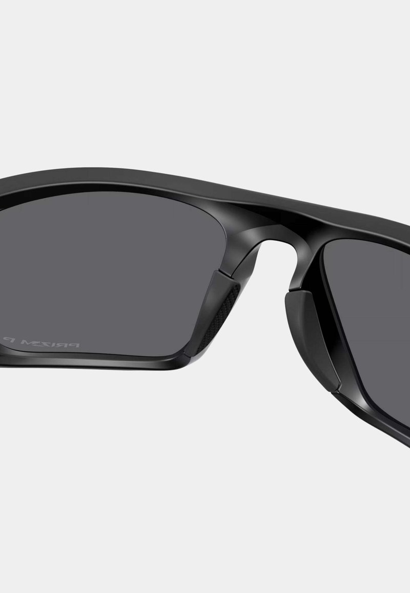 Lunettes de sport noires au design élégant et anguleux, avec des verres foncés et des accents en caoutchouc texturé sur les branches pour une meilleure prise en main et un confort optimal.