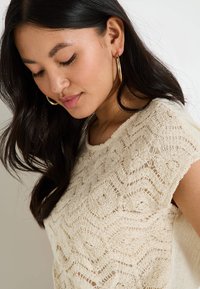 Top de punto color crema con intrincado patrón de encaje floral, mangas cortas y un corte relajado, con un acabado texturizado.