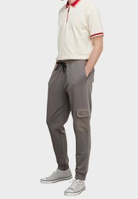 Graue Jogginghosen aus weichem Stoff, mit elastischem Bund und Kordelzug, seitlichen Taschen und einem Patch mit bedruckten Details.