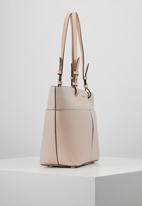 Beżowa skórzana torba tote o usztywnionym kształcie, z podwójnymi uchwytami u góry i złotymi akcentami metalowymi. Posiada teksturowaną powierzchnię i kontrastujące czarne szwy.